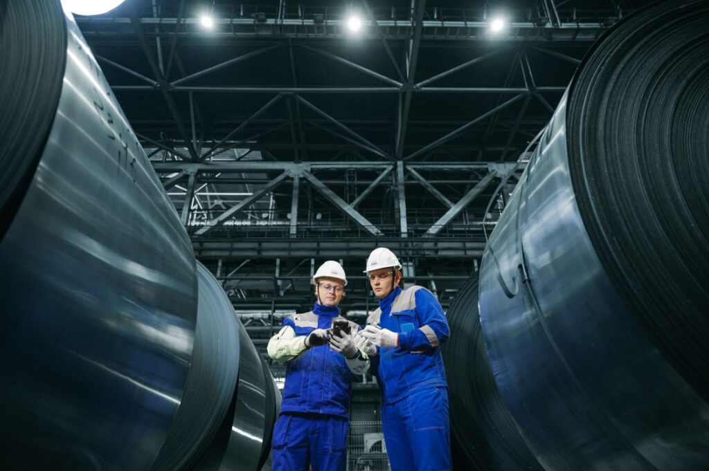 Two workers inspecting steel between large coils